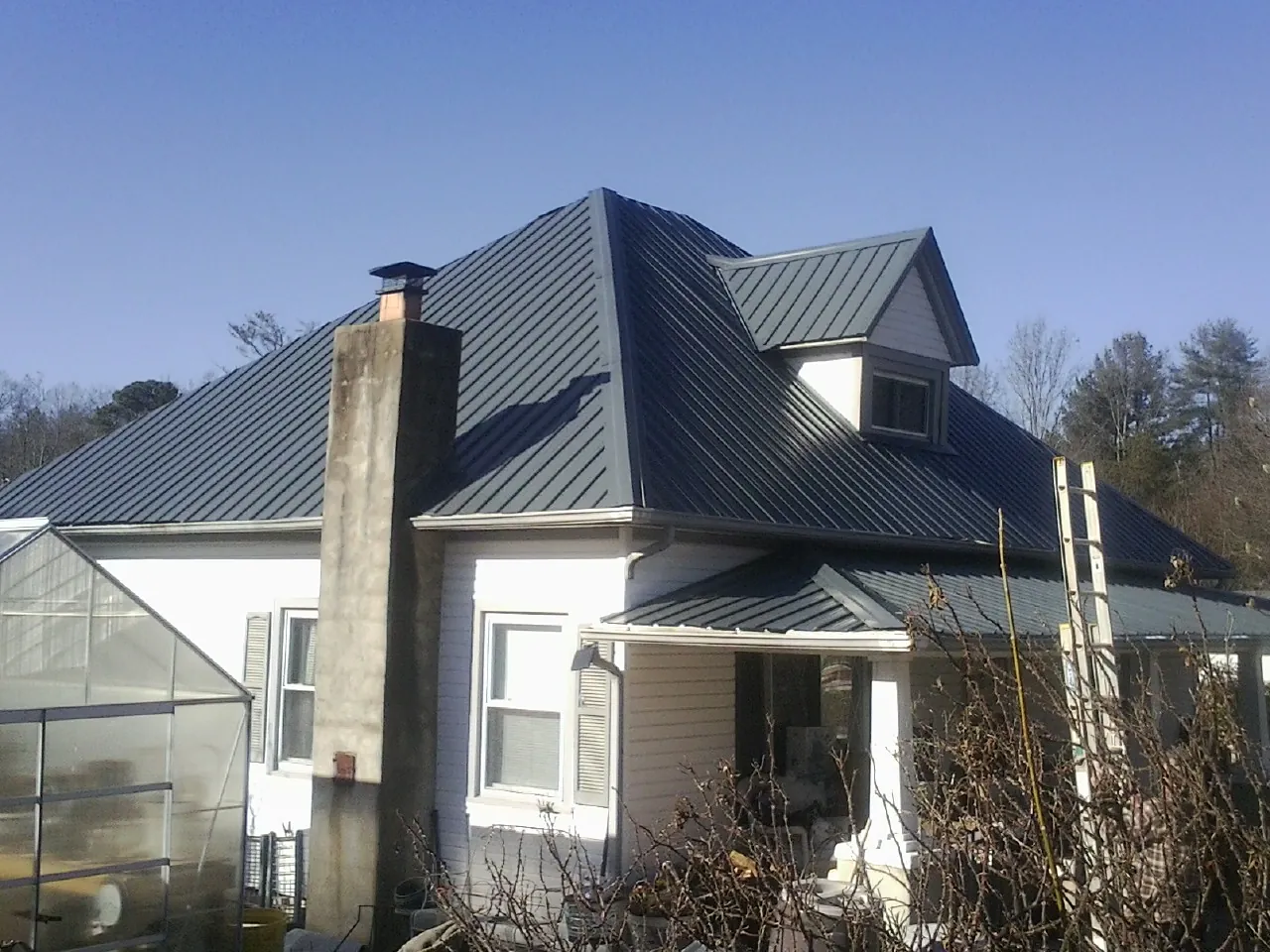 Dark blue standing seam metal roof on a white farmhouse with dormer — Slate & Tile Roof Repair by Roofing Brothers in Spiritwood