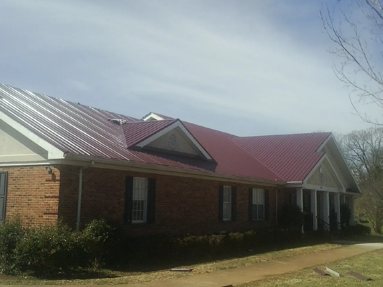 Red metal roof with gabled entries on a long brick building, from a Hail Damage Roof Repair job in Spiritwood