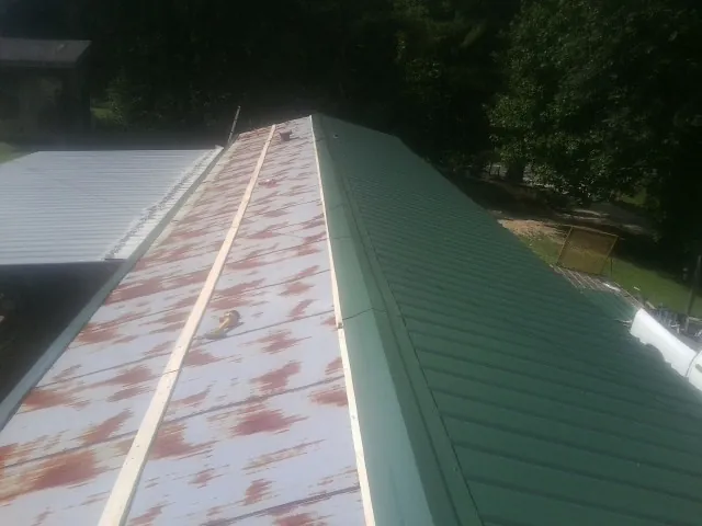 Old rusted panels beside newly installed green metal roofing — Wind Damage Roof Repair by Roofing Brothers in Spiritwood