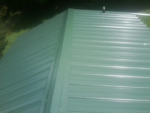 New green metal panels meeting at the ridge of a roof — Flat Roof Repair work by our crew in Spiritwood