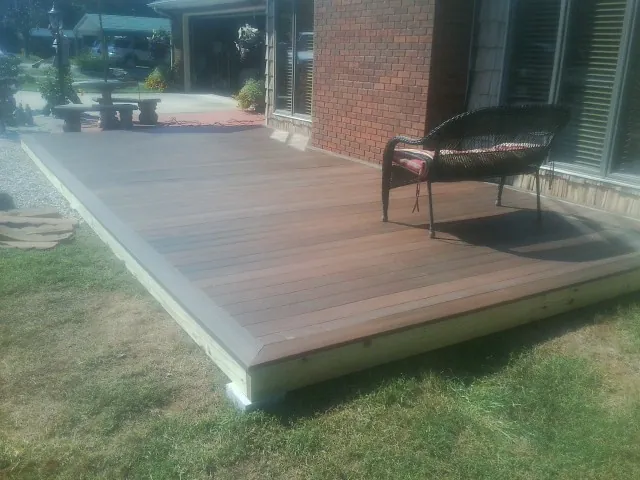 New wood deck and wicker chair beside a brick house in Spiritwood