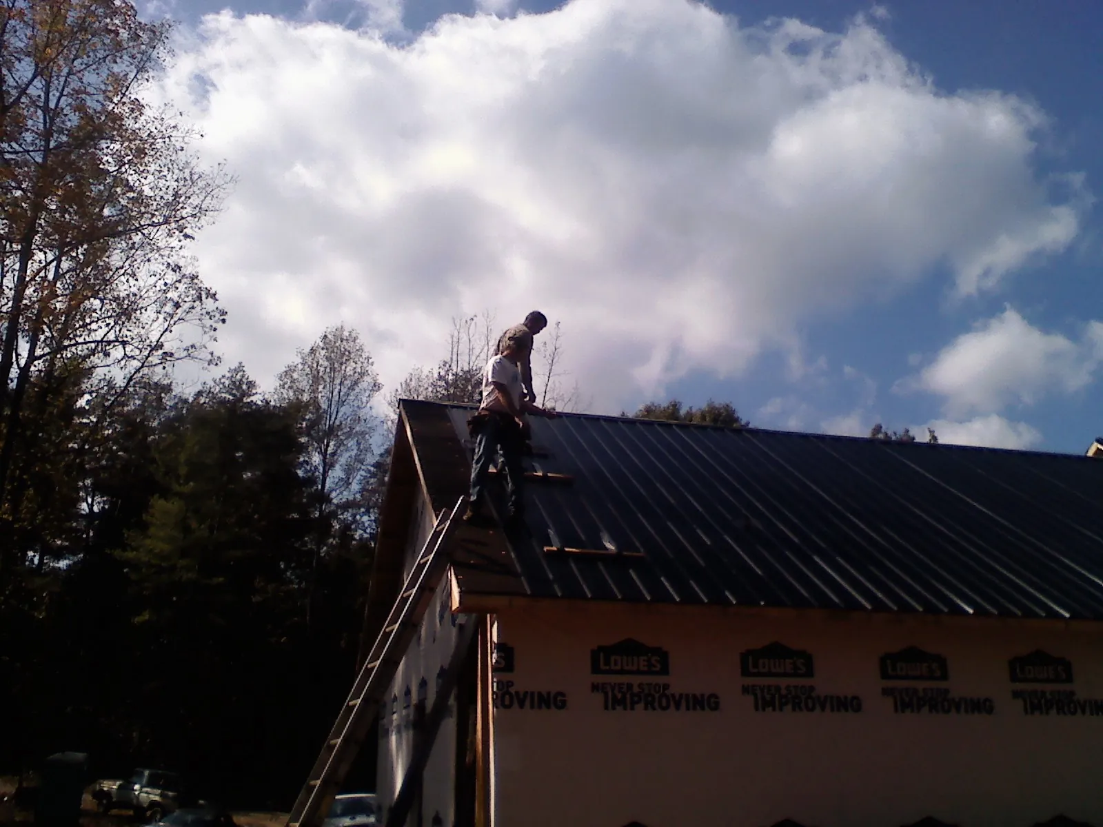 Roofer fastening dark metal panels high against a cloudy sky, from a Roof Inspection job in Spiritwood