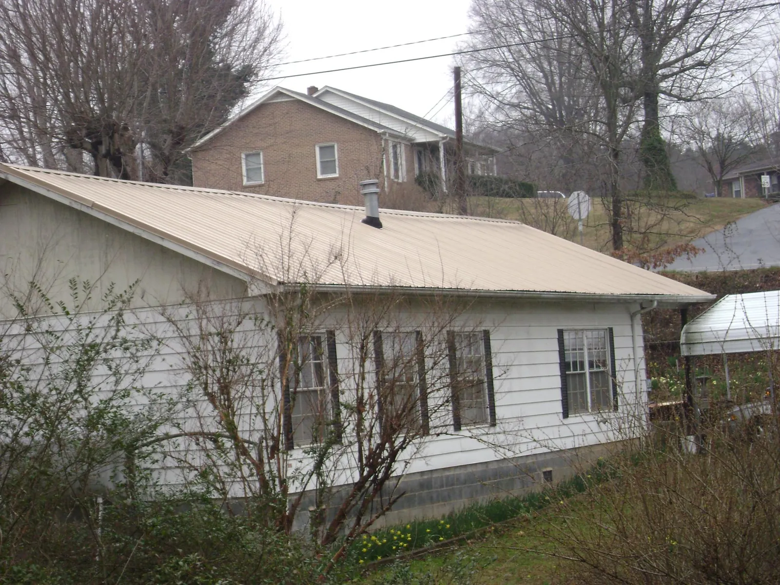 Tan metal roof on a white sided house set into a hillside — Commercial Roofing by Roofing Brothers in Spiritwood