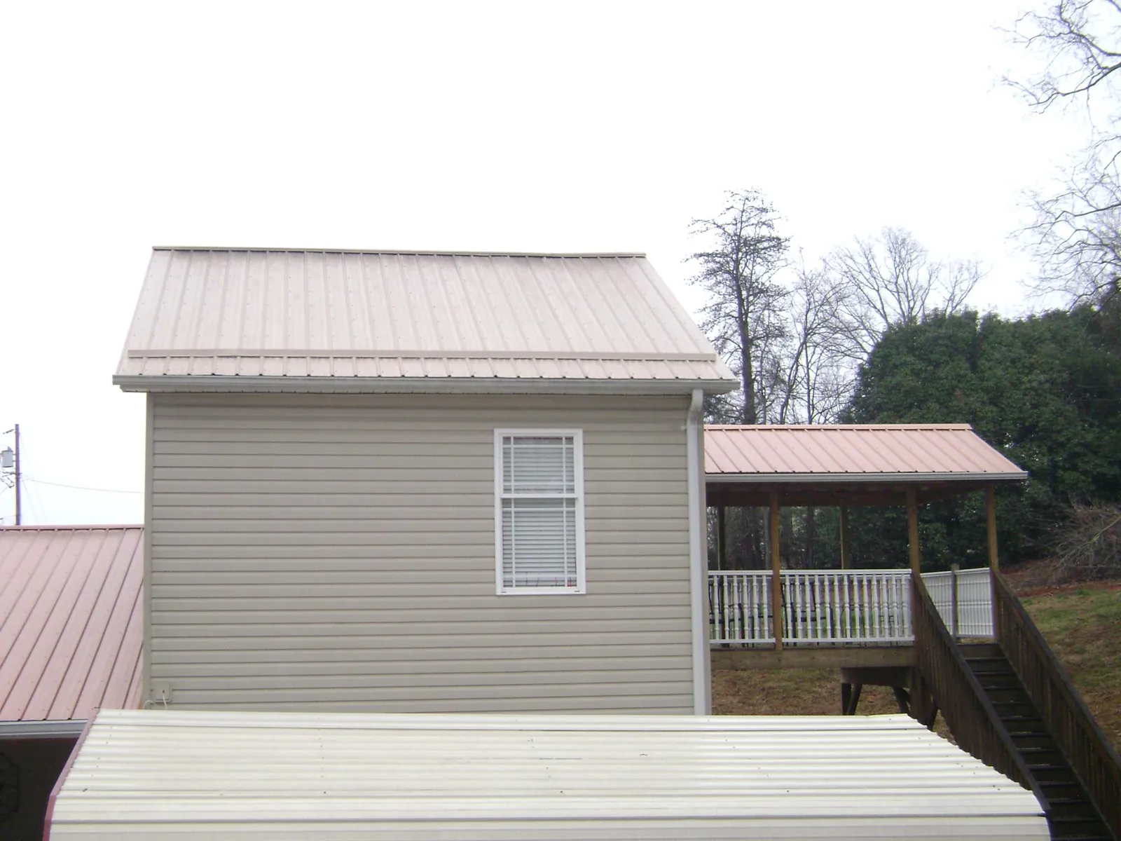 Tan metal roofs on a two story addition and attached porch, from a Roof Replacement job in Spiritwood
